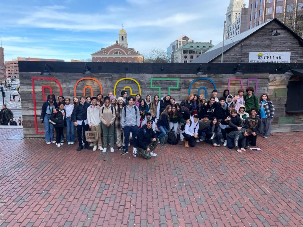 Fieldston Upper students pose in front of sign outdoors on their field trip to Boston.
