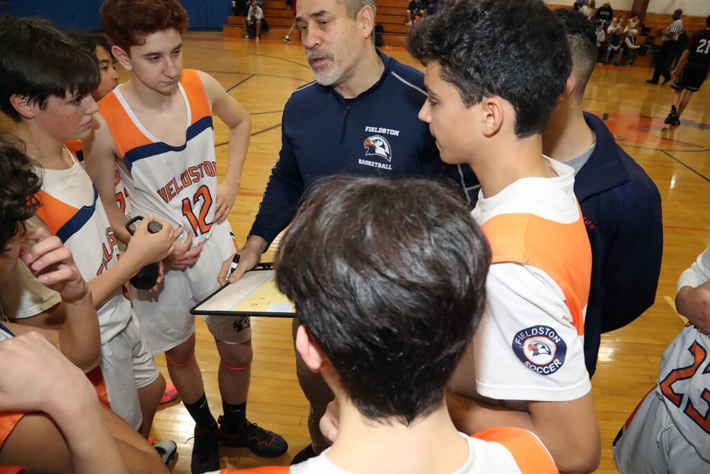 Fieldston Upper JV boys basketball team huddles around coach to hear play call.