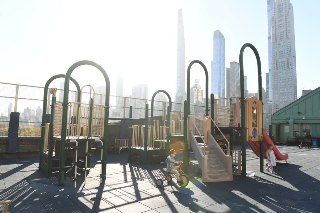 Scenic shot of the Ethical Culture 6th floor rooftop playground; New York City skyline can be seen peeking behind the jungle gym.