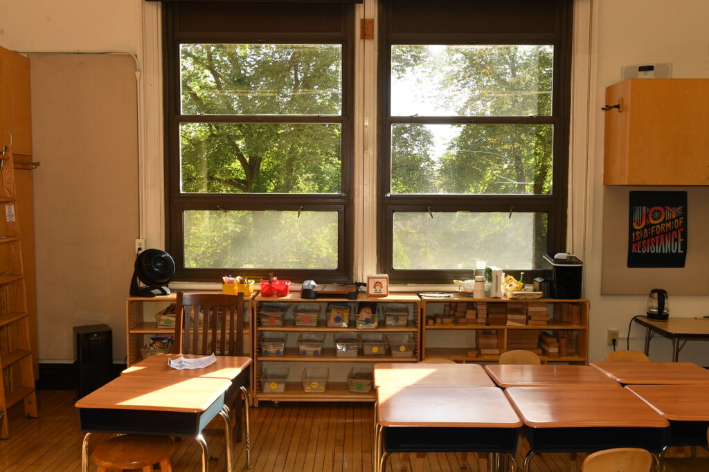 Indoor photo of Ethical Culture classroom. Desks sit in the foreground, and windows overlooking Central Park fill the background.