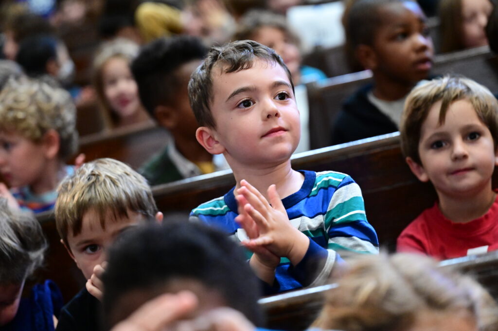 Young Ethical Culture student claps in audience in auditorium.