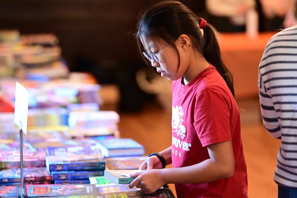 Student stands in front of table of books, looking at one in particular, at the Ethical Culture Book Fair.