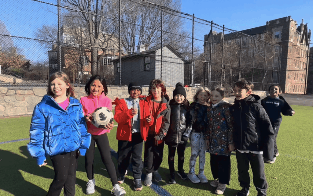 A group of 2nd Grade Ethical Culture Fieldston School students from Fieldston Lower stand smiling together smiling