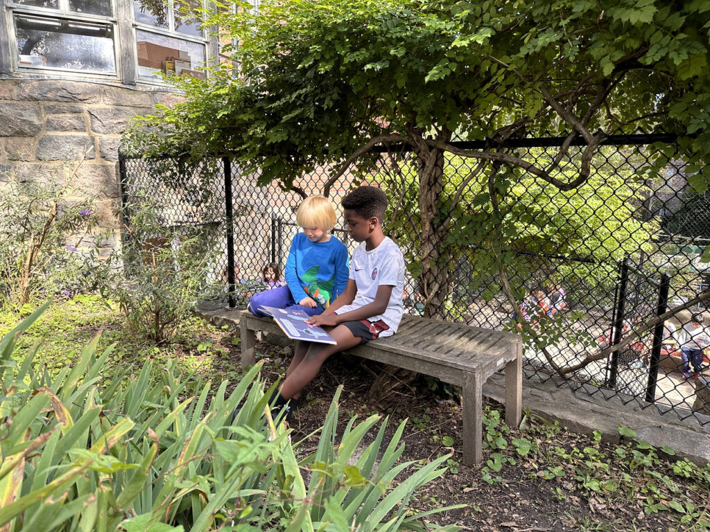 Two Fieldston Lower students read together on a bench outside.