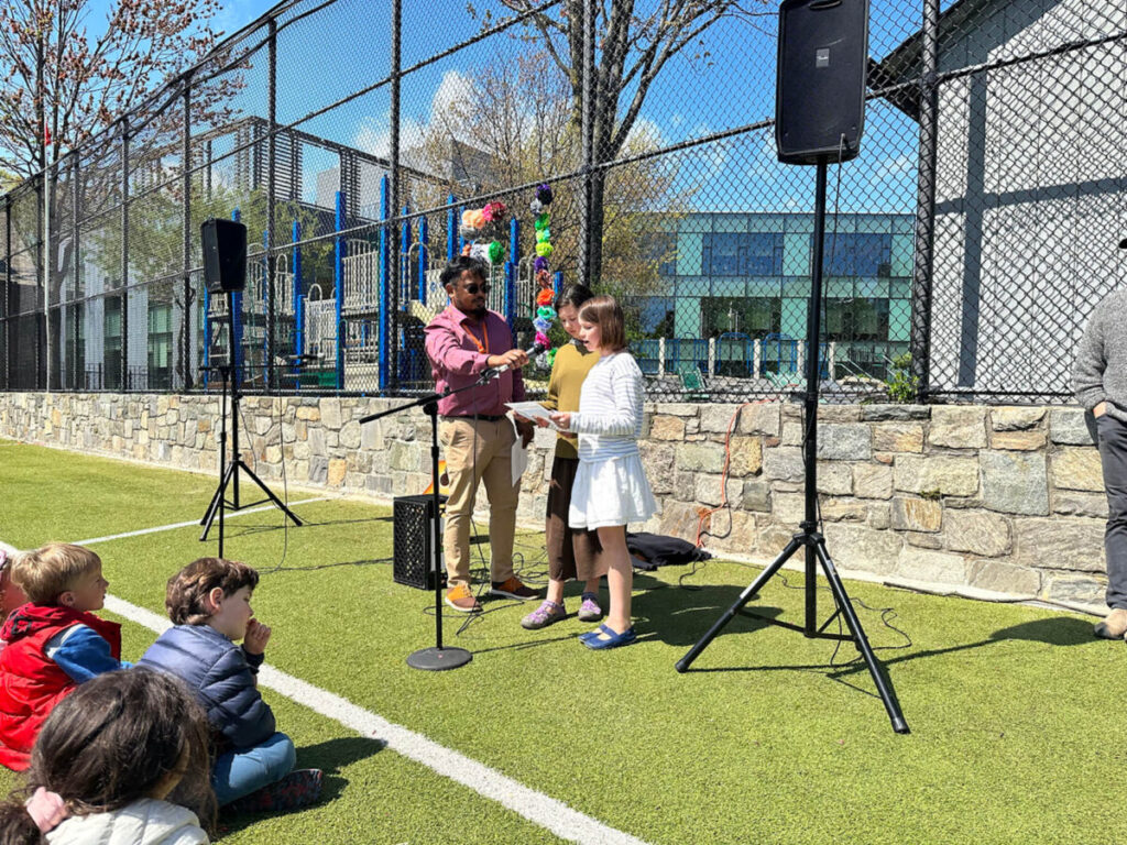 Fieldston Lower Assistant Principal Shawn Chisty holds a microphone for two 5th Grade Students who are speaking at the Earth Day assembly.