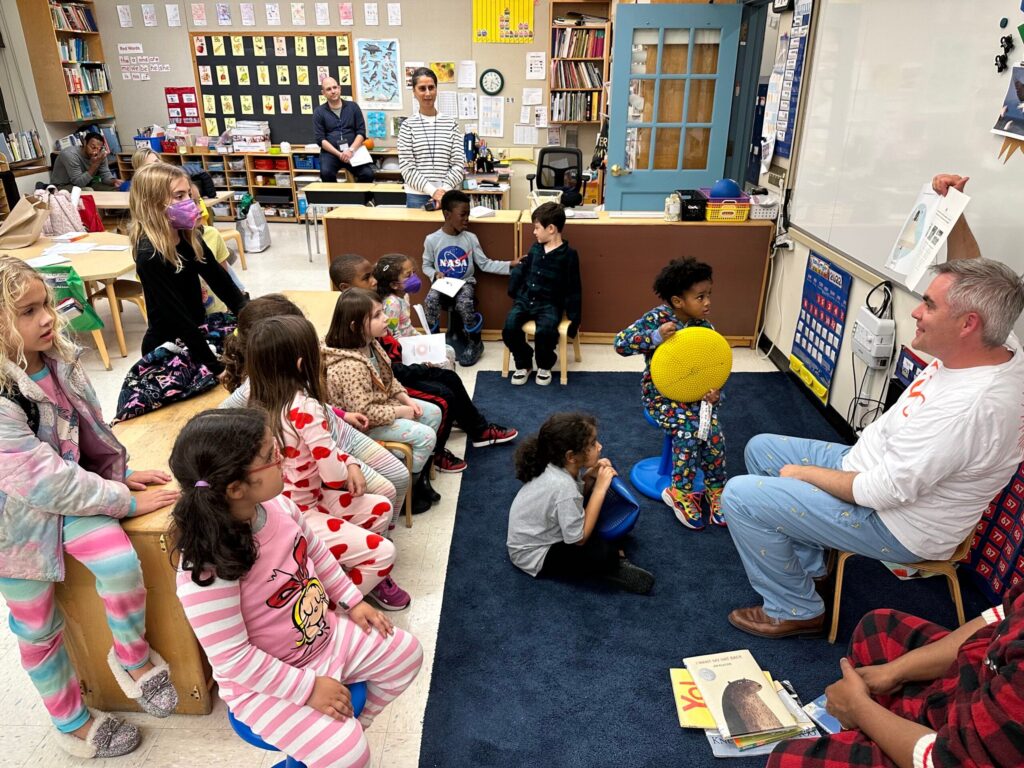 Fieldston Lower Principal Joe McCauley reads to a room full of students; they sit on the floor in pajamas and listen along.