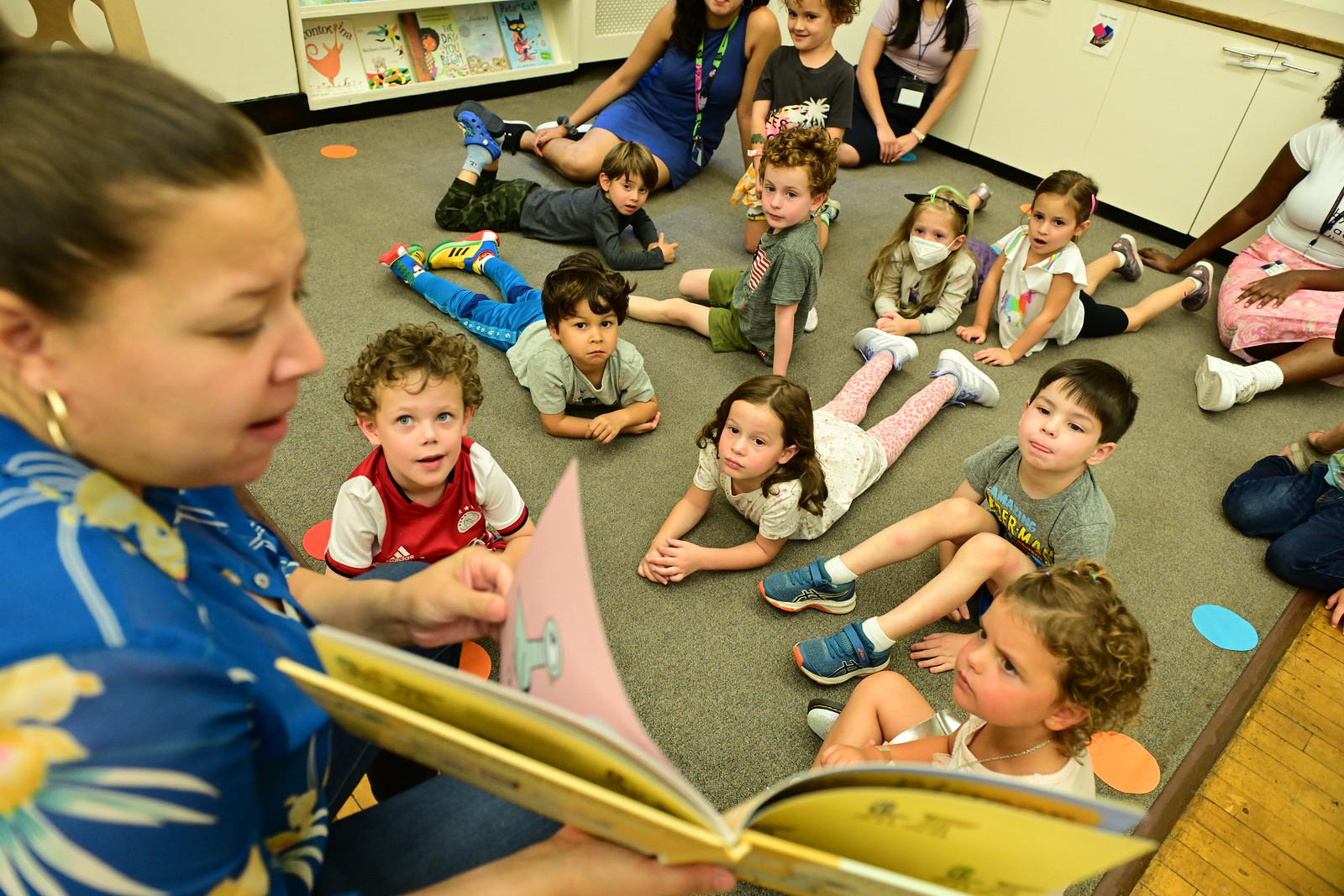 Ethical Culture's youngest learners listen on carpet as teacher reads from a book. 