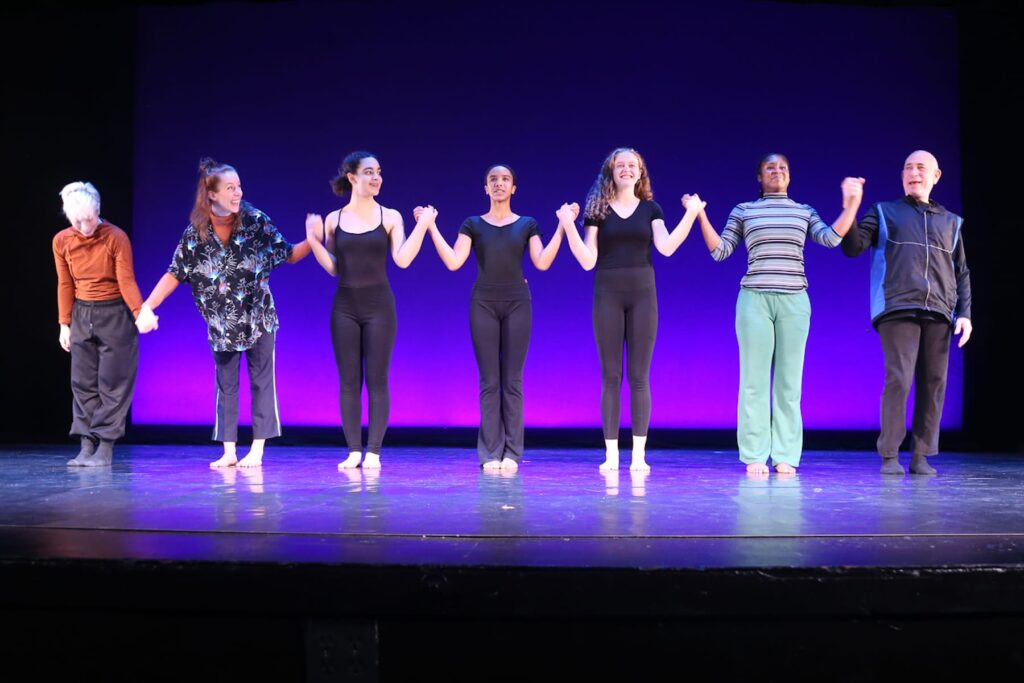 Dancers hold hands in a line and prepare to take a bow on stage.