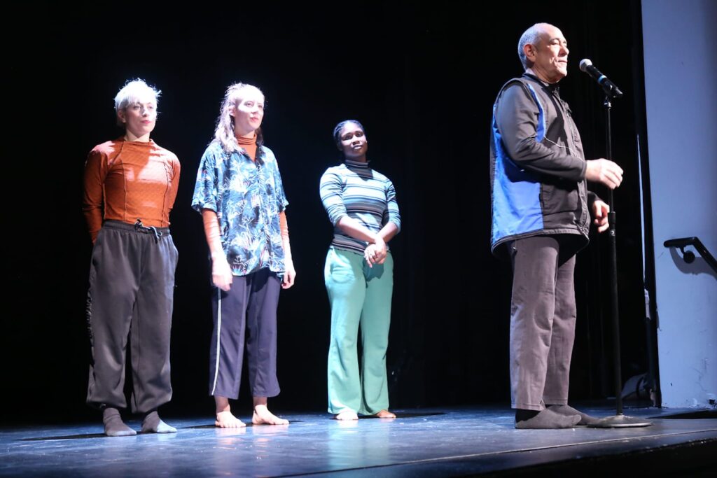 David Dorfman introduces piece at the microphone while his dancers look on in the background.