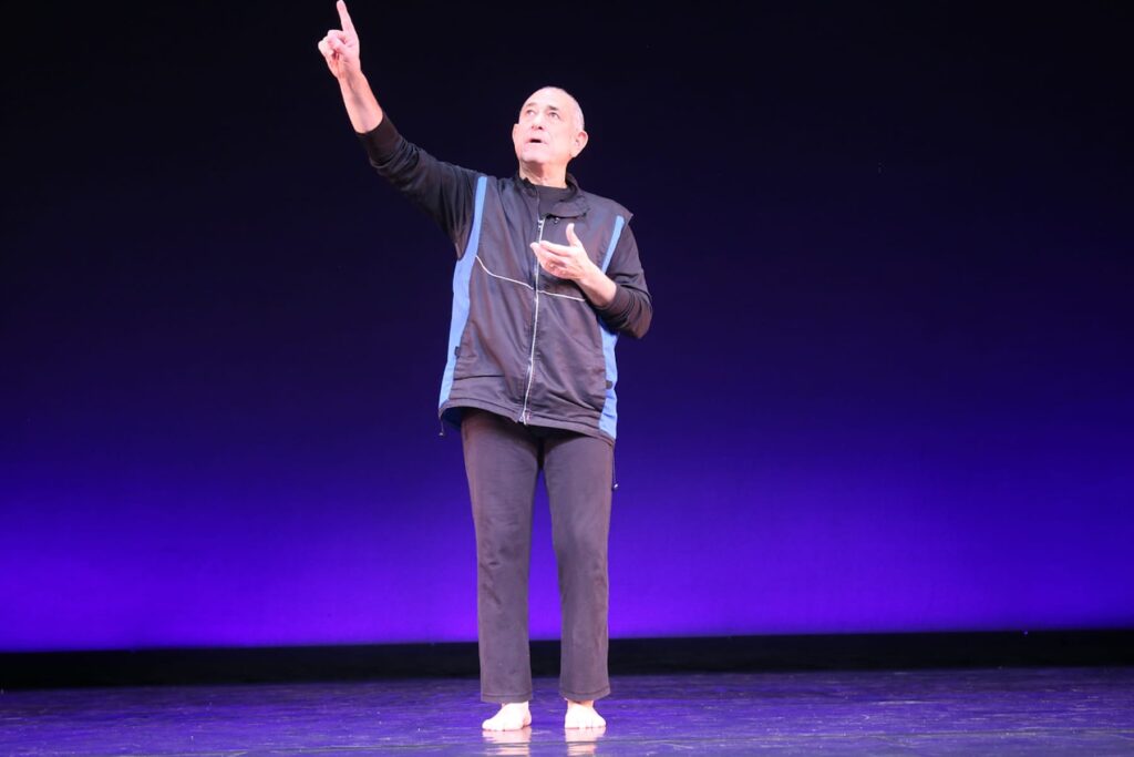 David Dorfman on stage, one hand pointed toward the ceiling.