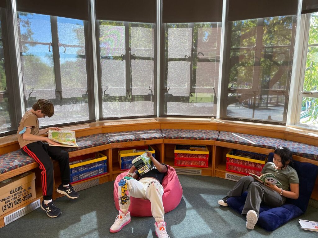 Three students sit and read in front of the windows of Fieldston Lower library